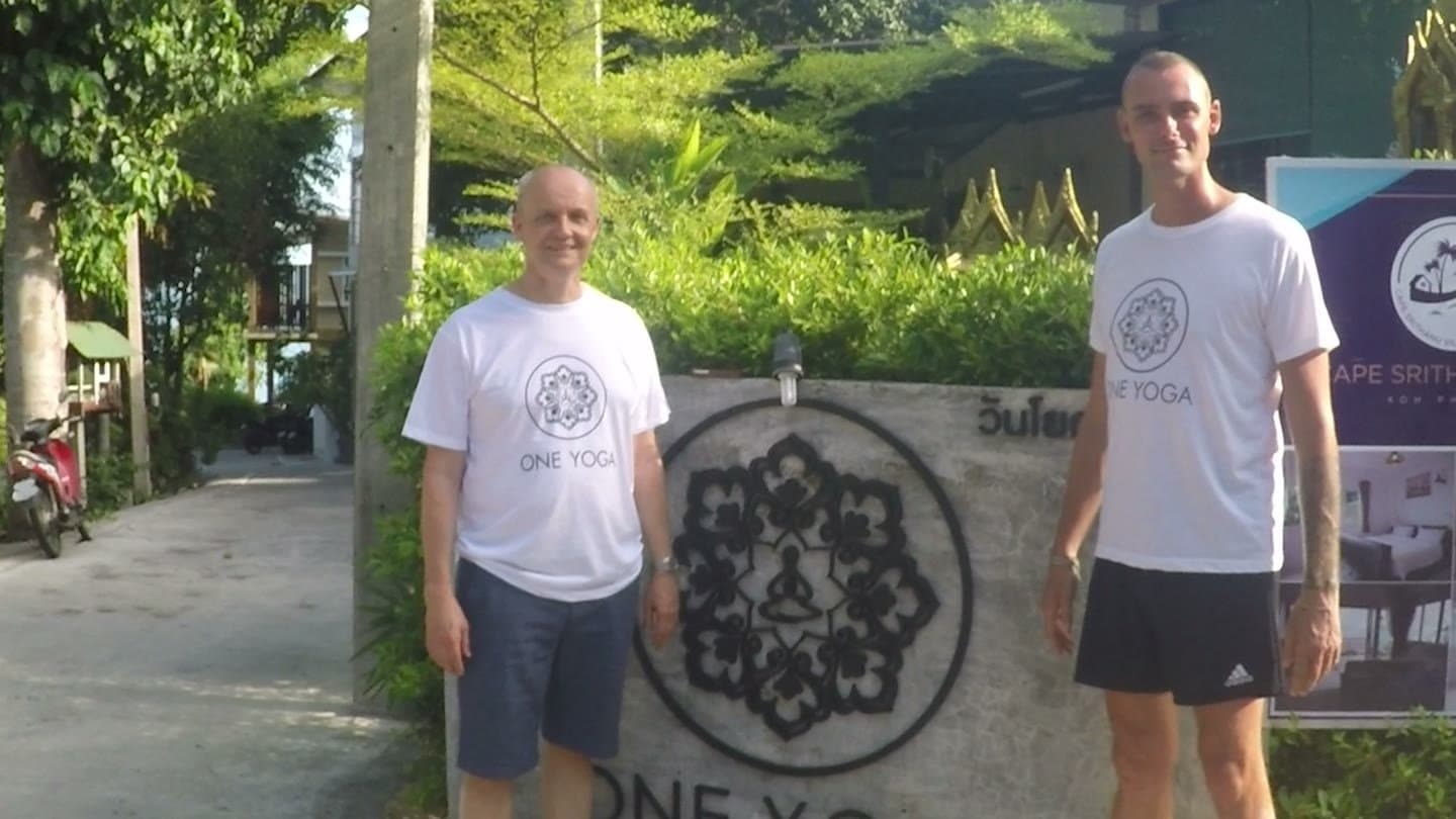 Henrik and Danny in One Yoga t-shirts, standing either side of the One Yoga sign at their resort.